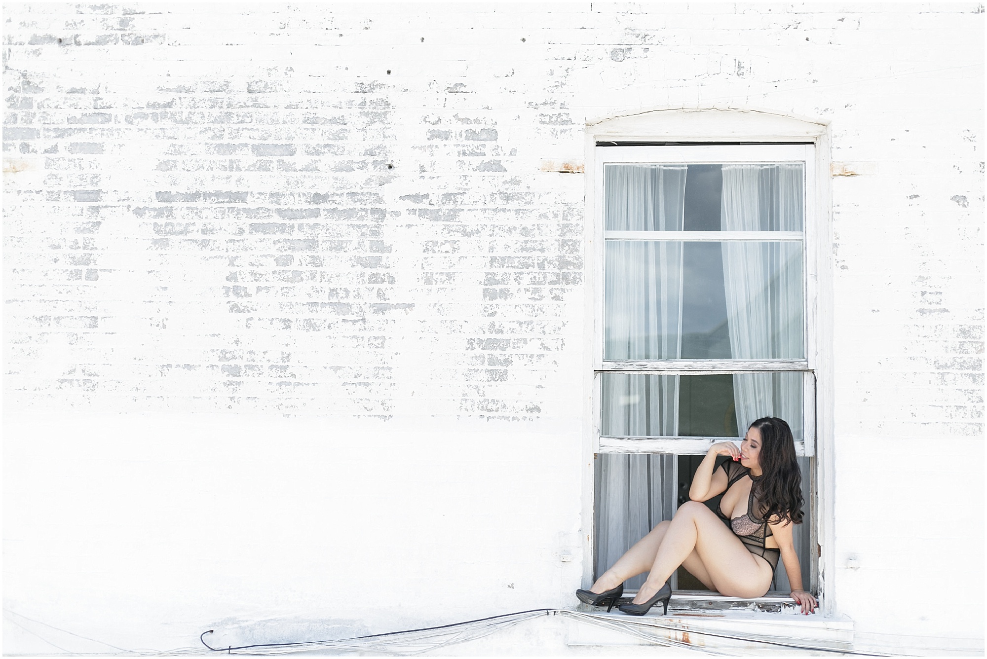 Model sitting on a window sill in black lingerie and black heels. 