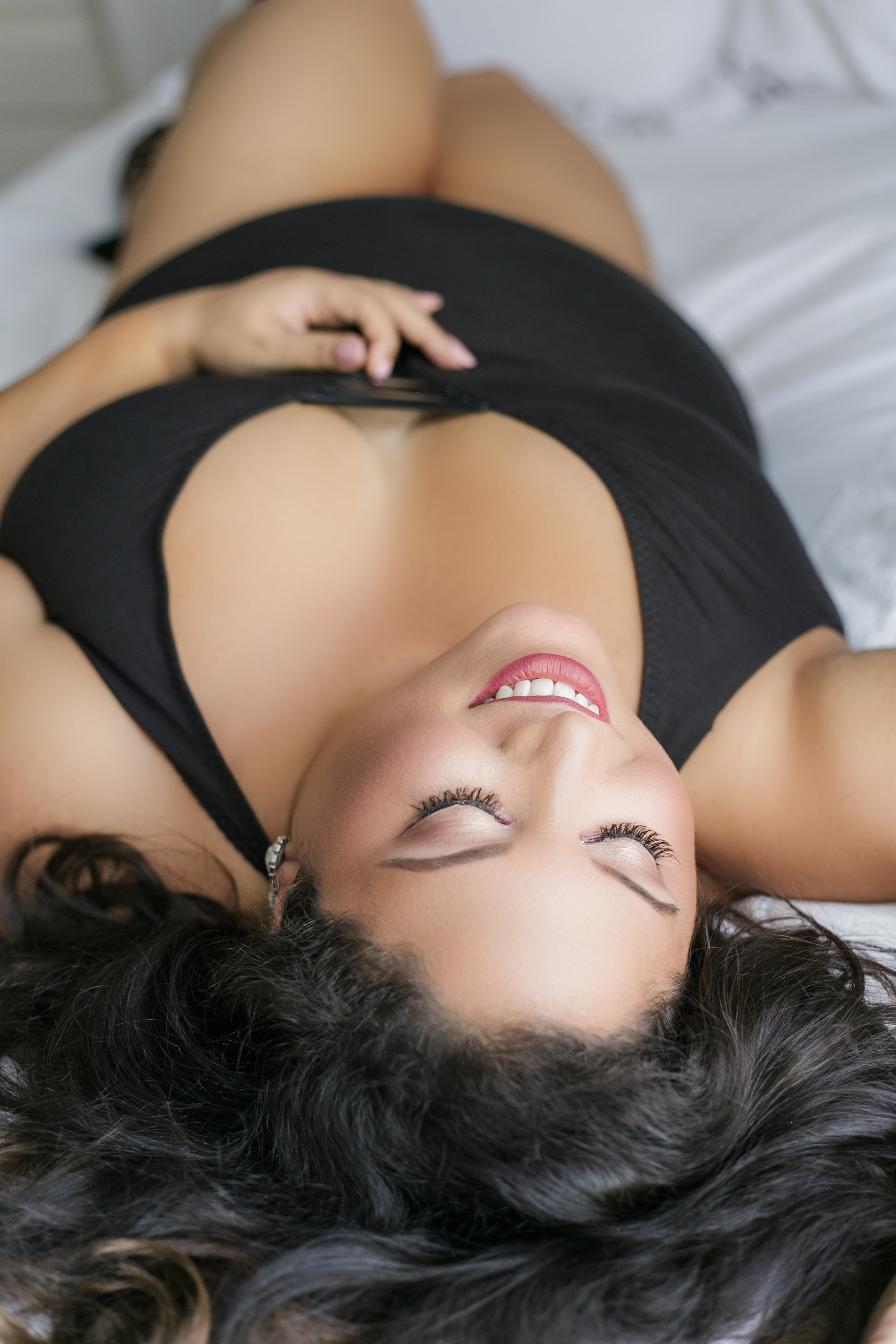 Model laying down on the bed wearing a black bodysuit.