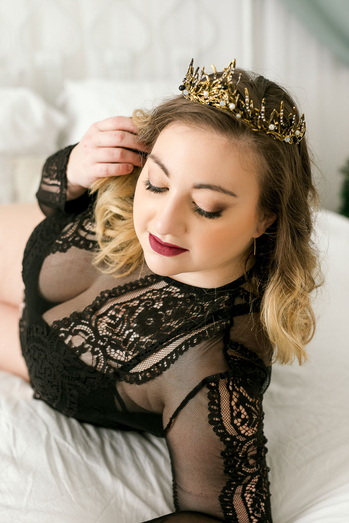 Woman wearing a gold crown and wearing a black lace outfit at boudoir session