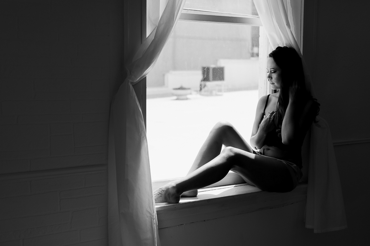 Black and white photo of a lady sitting on a windowsill for boudoir photos