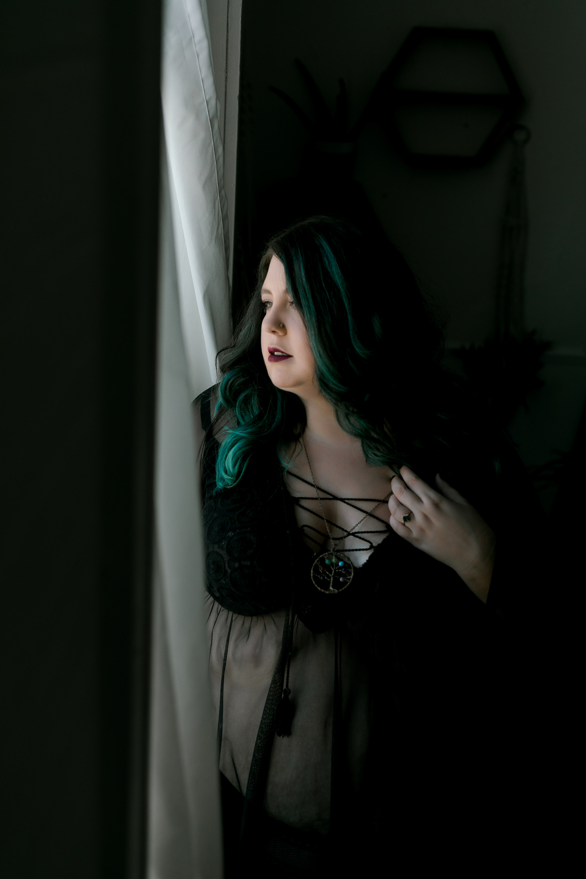 Woman with green hair highlights standing next to the window in black lingerie. 