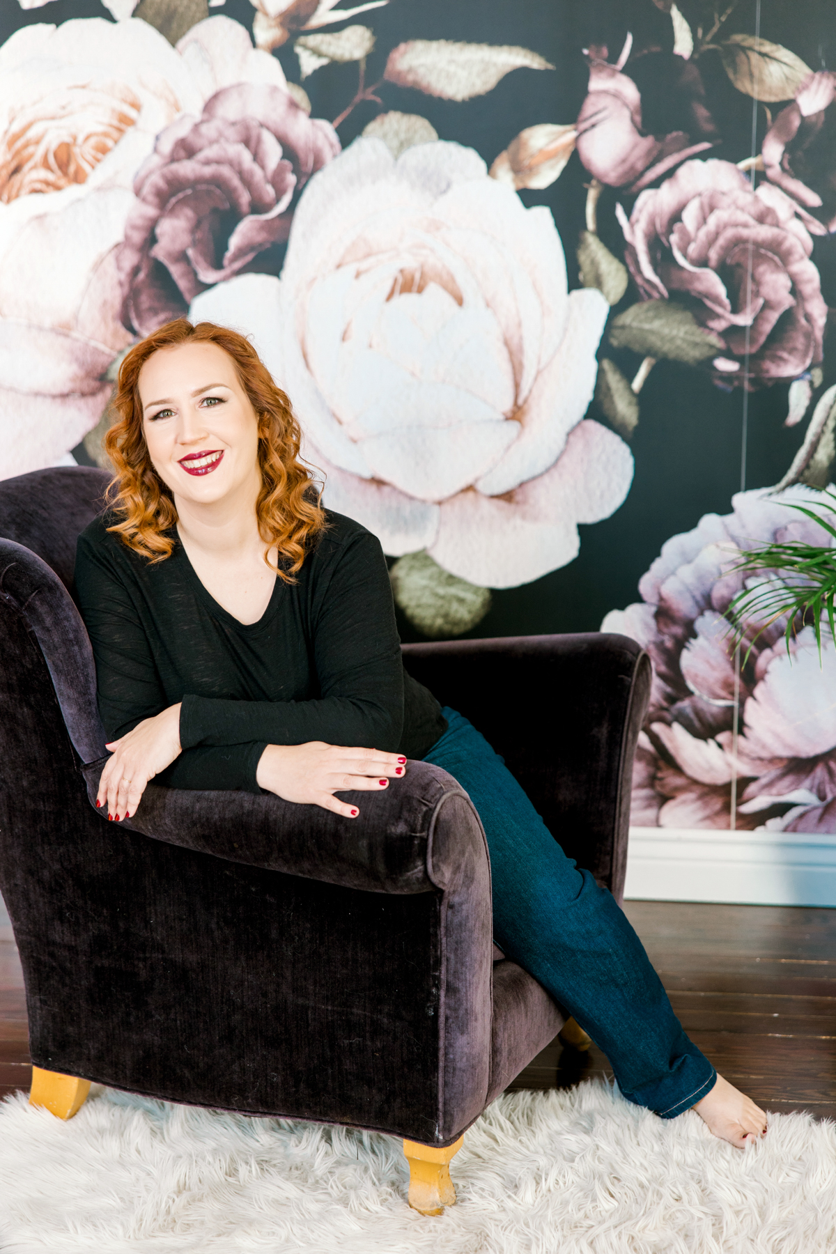 woman with red hair on purple chair with floral wall 