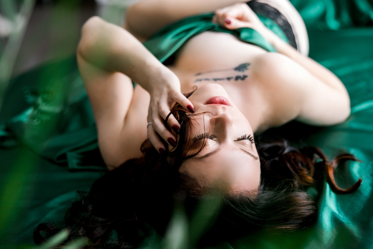 Woman posing covered up by green satin sheets and wearing black panties