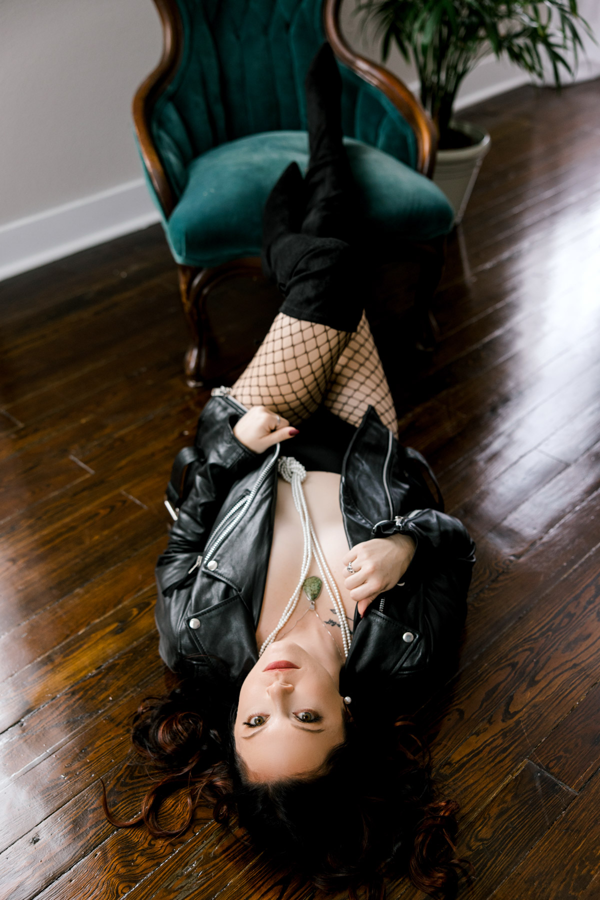 Woman laying on the floor wearing black leather jacket, fishnet stockings and accessories. 