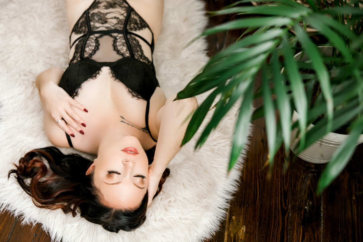 Woman laying on the floor in black lingerie with neutral makeup in gold tones. 