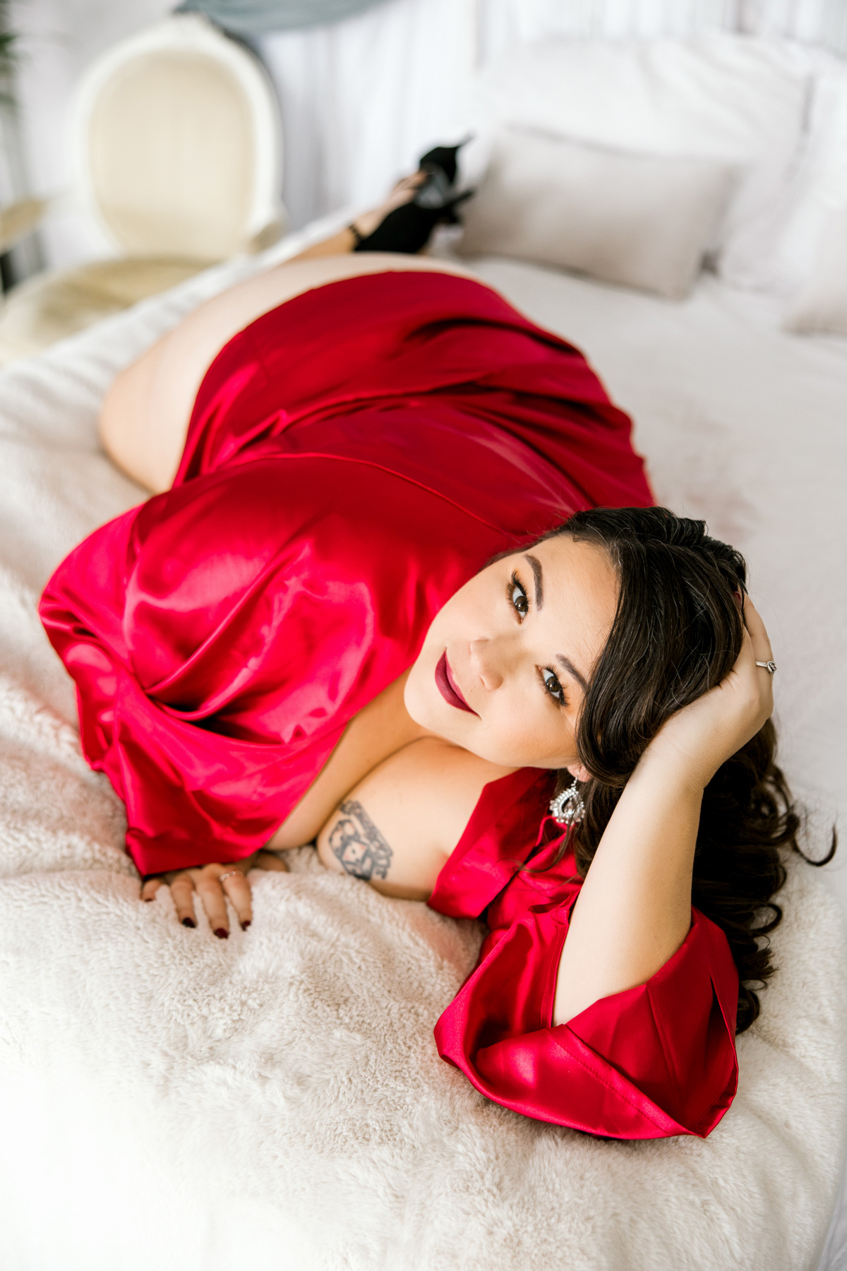 brunette on bed tattoo on chest laying down wearing red satin robe