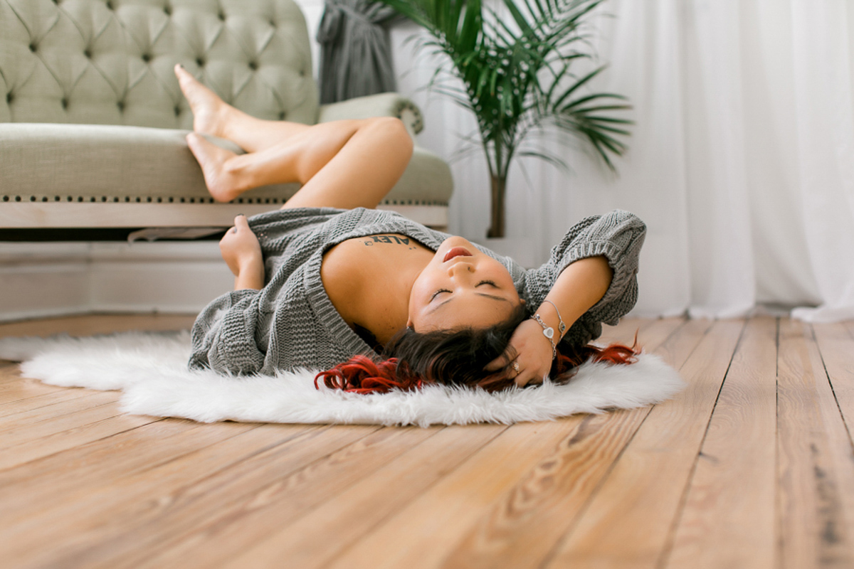 girl laying on rug in front of green sofa set with grey off-the-shoulder sweater