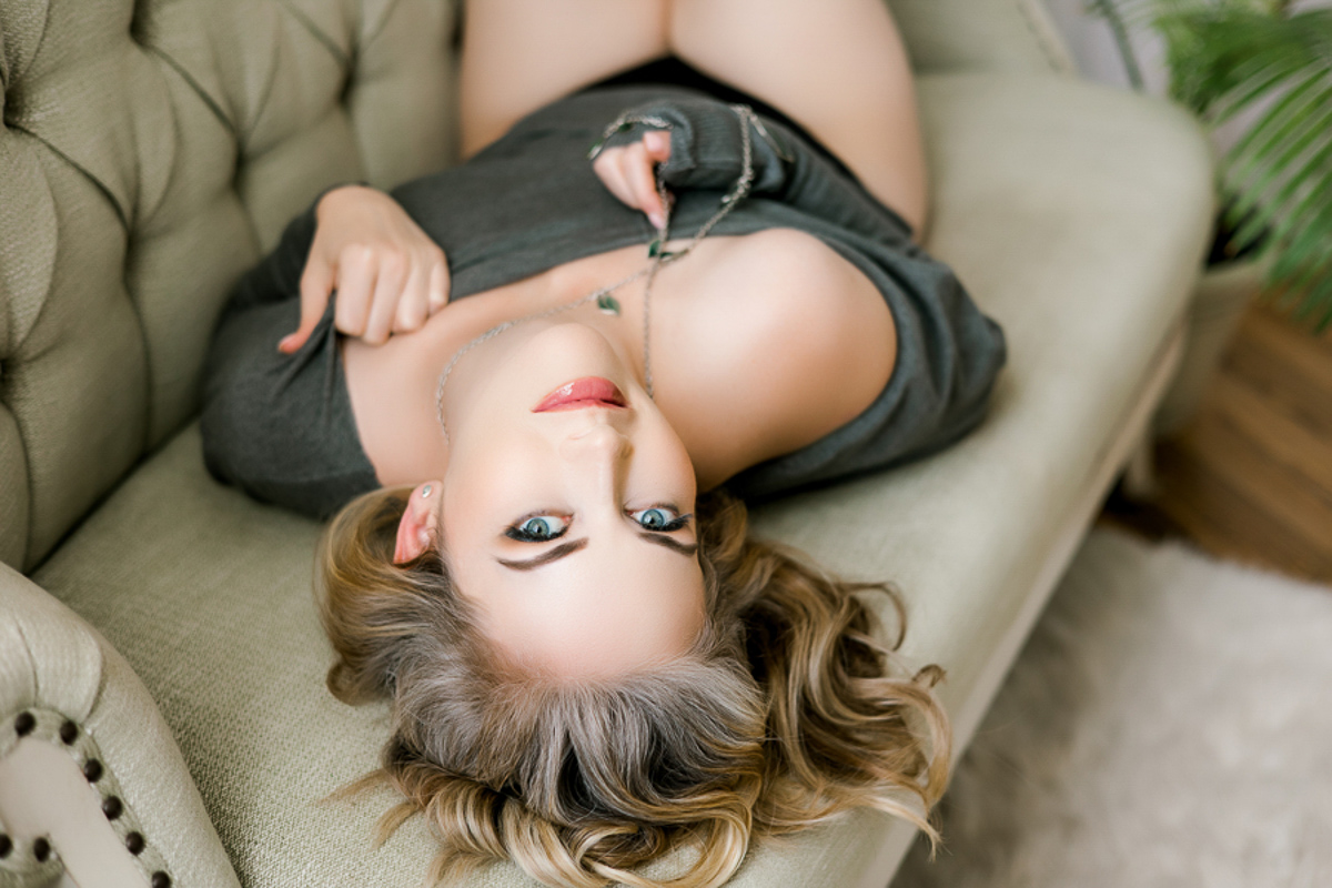 stunning girl in grey sweater and necklace laying on green sofa set