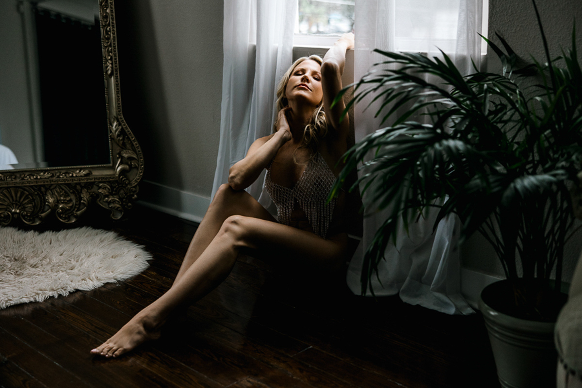 blonde woman sitting on floor in front of window in diamond bra