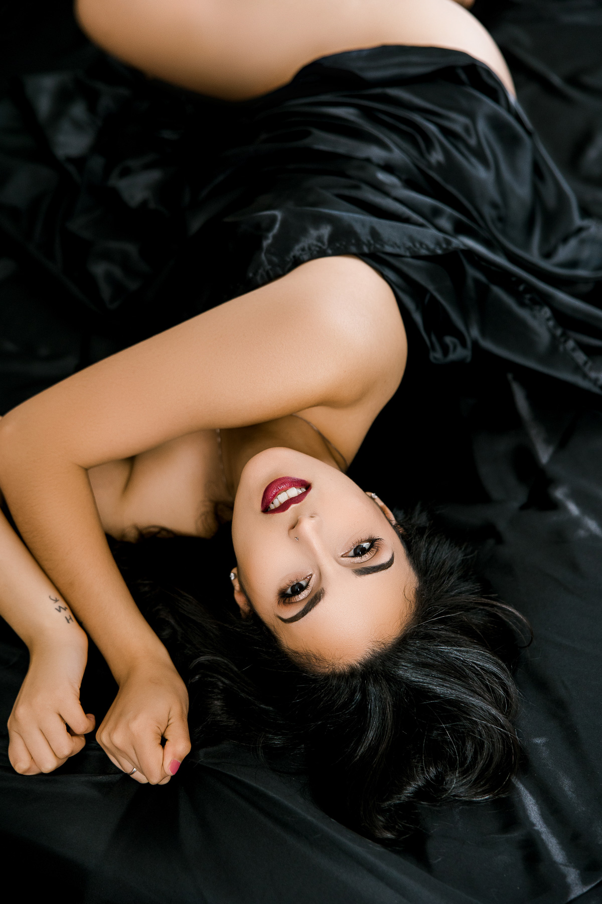 stunning woman with black hair and red lips tangled in satin bed sheets