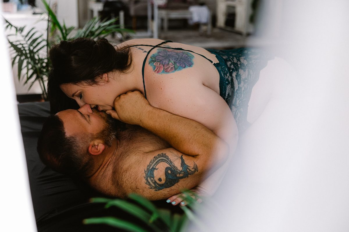 woman on top of man kissing on black bed set for couples boudoir session