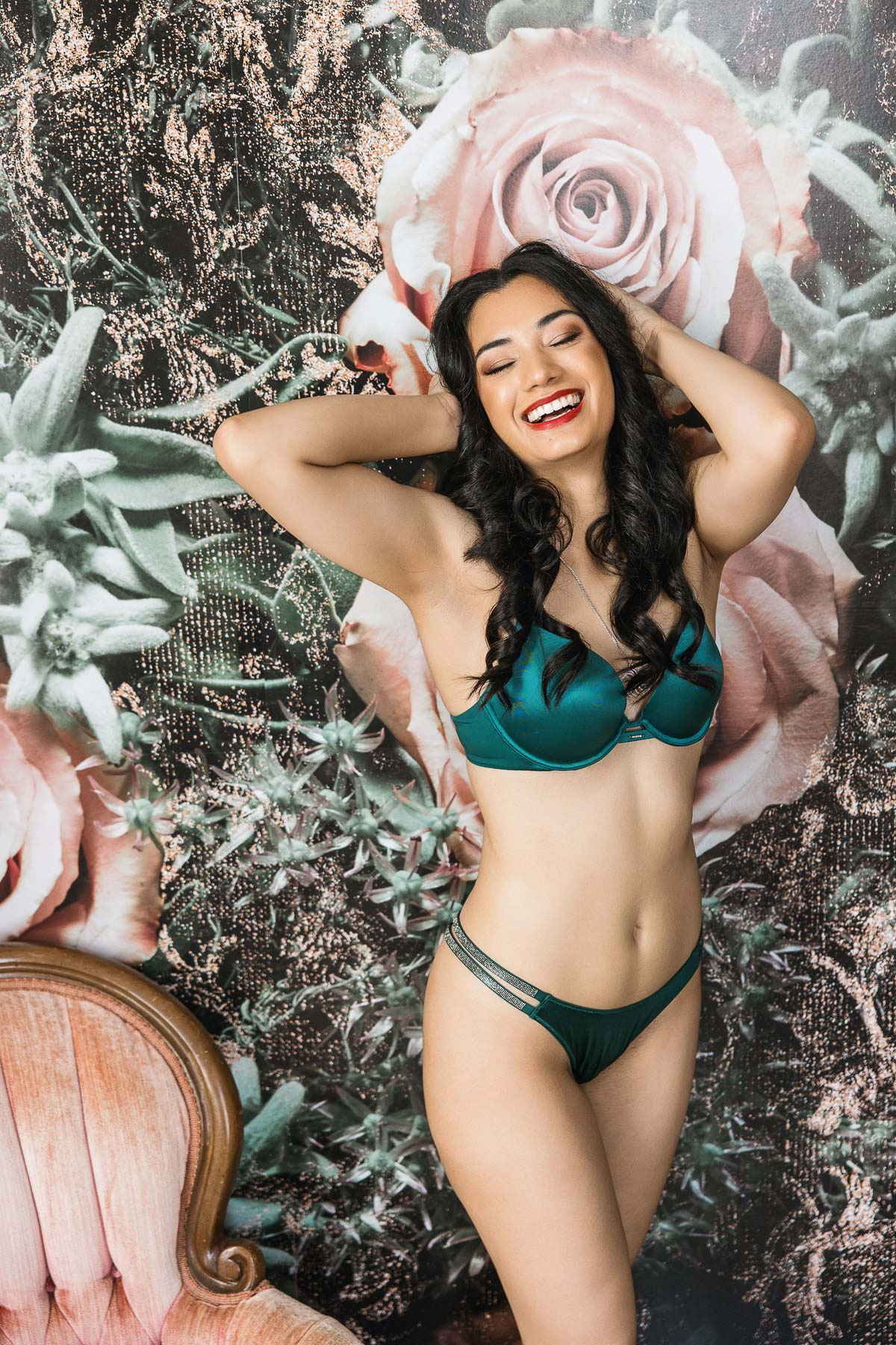 Woman in bra panty set laughing leaning up against floral wall