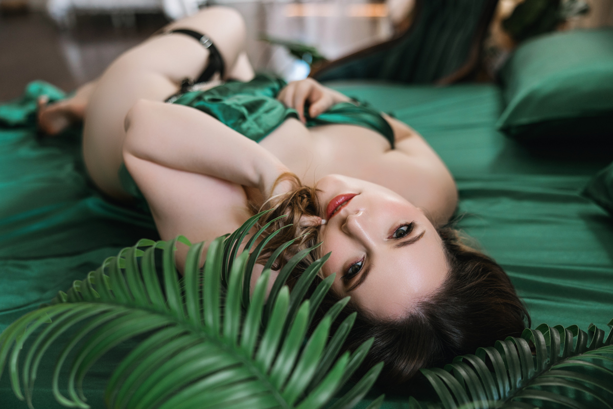 woman wrapped in green satin sheets hand in hair looking at camera 